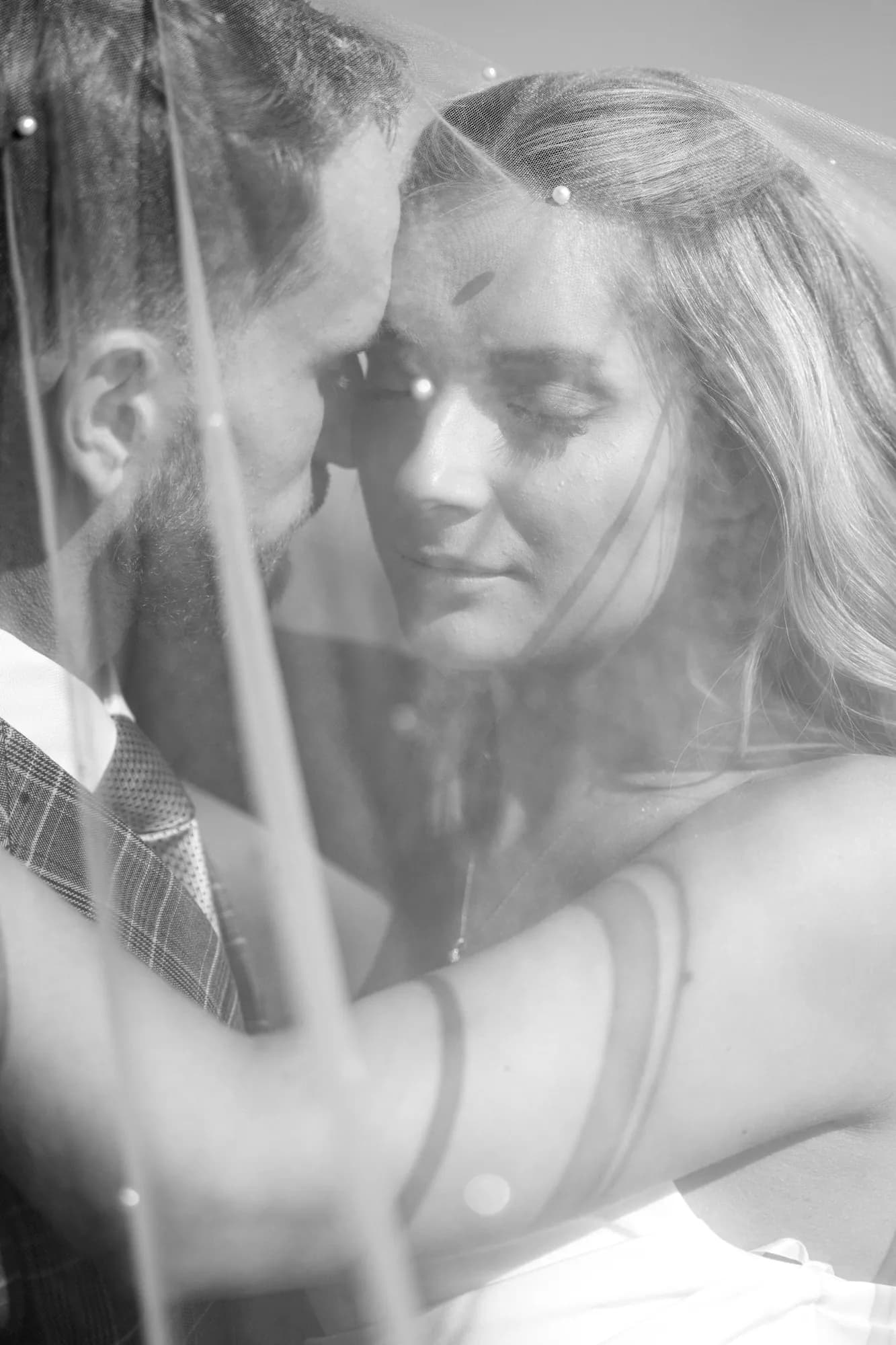 Black and white portrait of a bride and groom close together beneath a veil